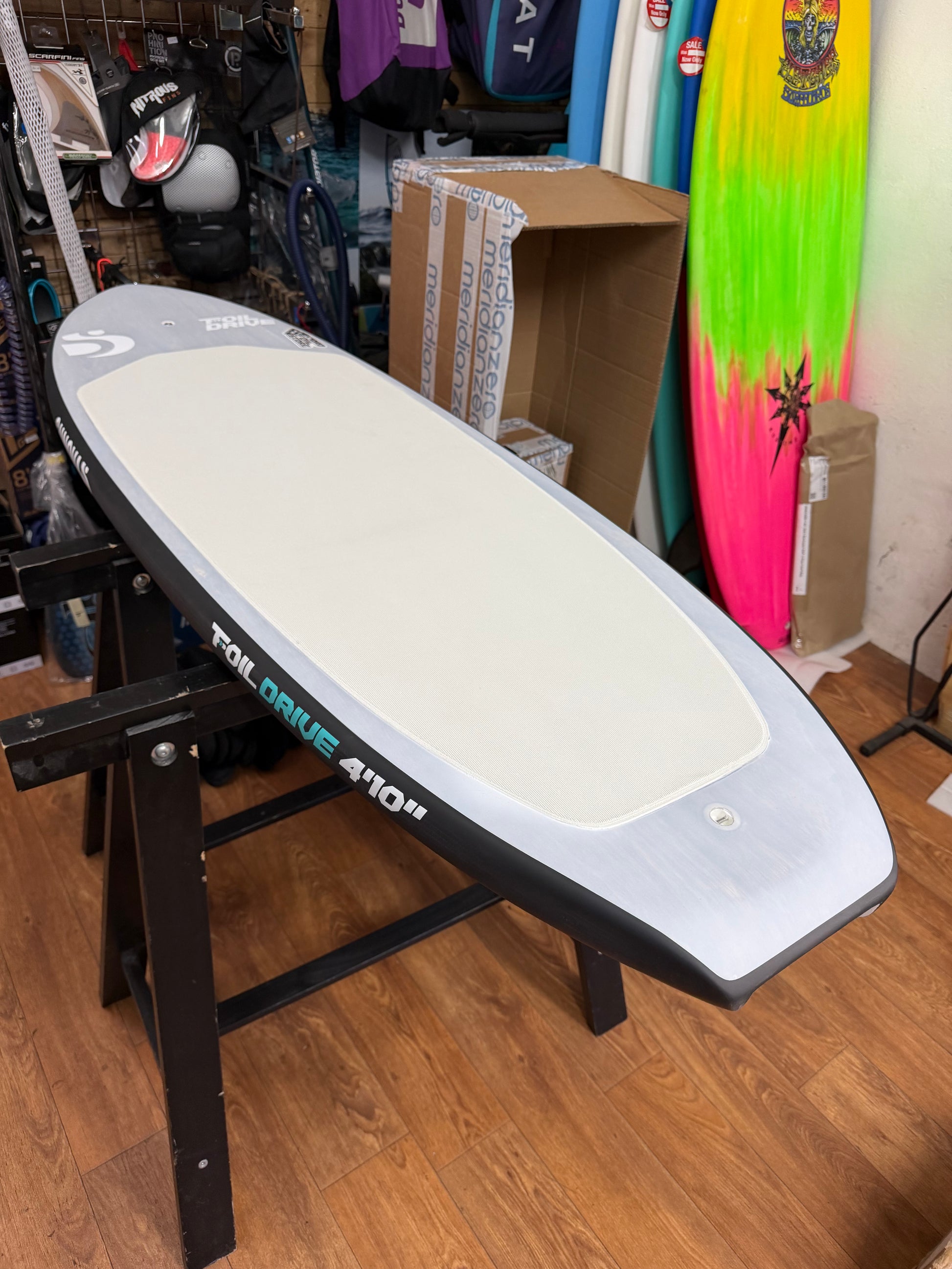 Foil drive surfboard on a stand in a store setting with various items in the background